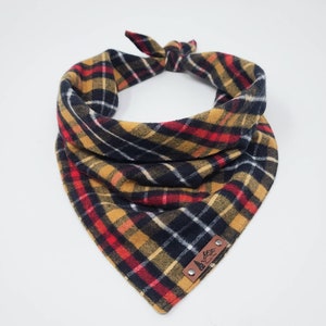 May include: A plaid bandana in black, red, yellow, and white with a brown leather patch that says "Mountain Life" in white lettering.