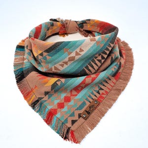 May include: A brown bandana with a geometric pattern in shades of blue, red, orange, and yellow. The bandana has a fringed edge and a leather patch with the text "The Wild West" in black.