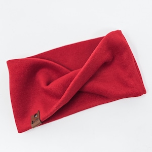 May include: A red fabric headband with a brown leather tag. The headband is twisted and folded, creating a unique and stylish look.