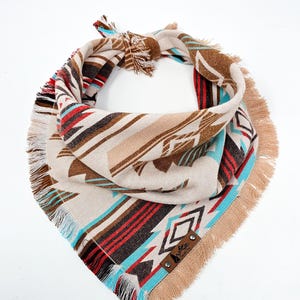 Könnte beinhalten: Ein Bandana in den Farben Beige, Blau, Rot und Braun mit Fransen und einem Muster. Das Bandana hat ein Leder-Etikett mit dem Text "The Wild" darauf.