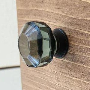 May include: A dark gray glass cabinet knob with a faceted design and a black metal base.