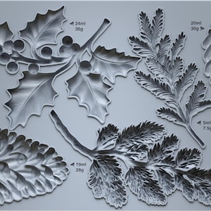May include: A gray silicone mold featuring various winter foliage designs, including holly with berries, pine needles, and pine cones. The text "IOD WINTER FORAGE" is printed on the top left corner. Measurements are indicated in milliliters and grams.