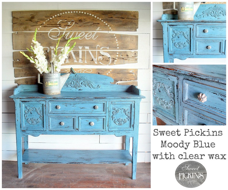 May include: A distressed blue painted sideboard with carved details and silver knobs. The sideboard has four drawers and a lower shelf. The sideboard is labeled "Sweet Pickins Moody Blue with clear wax".