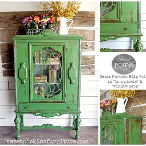 May include: A green antique cabinet with glass doors and a distressed finish. The cabinet has a drawer and sits on four turned legs. The cabinet is painted with Sweet Pickins Milk Paint in "in a pickle" and "window pane".