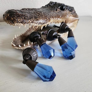 May include: Four blue glass cabinet knobs with a metal base. The knobs are shaped like a teardrop and have a shiny finish.