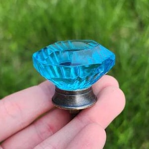 May include: A turquoise blue glass cabinet knob with a faceted design and a bronze base.