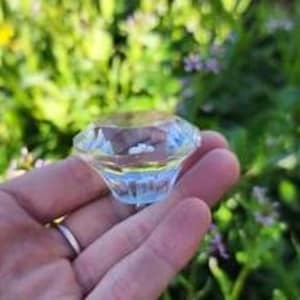 May include: A clear glass diamond-shaped knob with a beveled edge. The knob is approximately 1 inch in diameter.