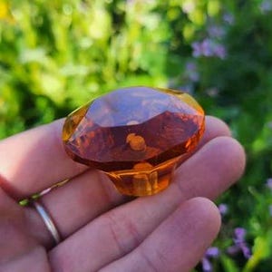 May include: A faceted amber glass knob with a hexagonal base. The knob is a vintage style and has a warm, honey-like color.