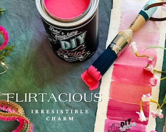 May include: A pink paint can with the text "Debi's design diary DIY Paint" and the phrase "Because you can." A paintbrush with pink paint on the bristles is next to the can. A white card with a pink paint swatch and the text "FLIRTACIOUS IRRESISTIBLE CHARM" is below the paint can and brush.