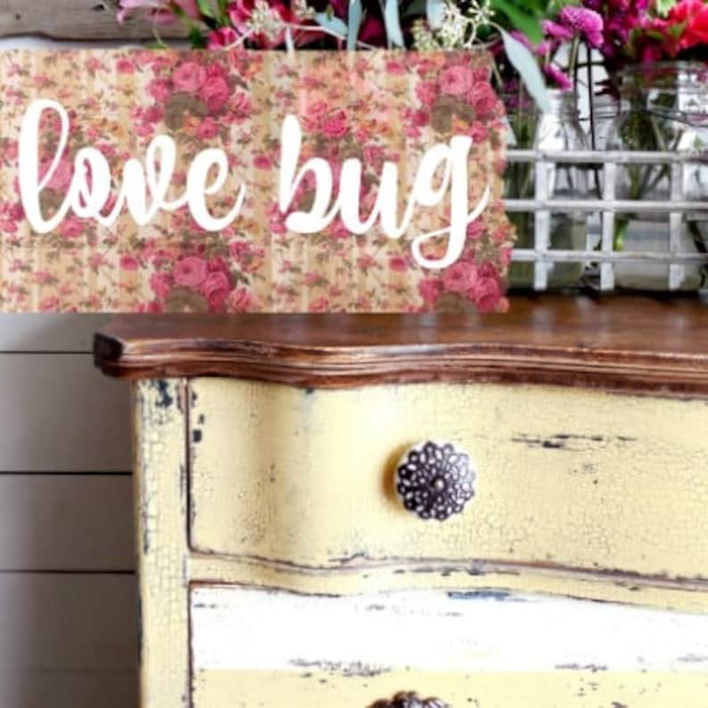 May include: A yellow painted dresser with a distressed finish and a floral patterned sign that reads "love bug".