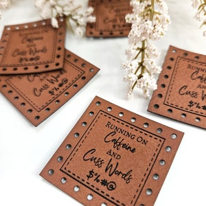 May include: Four brown leather patches with the text "Running on Caffeine and Cuss Words" and "$%#@" printed on them. The patches have a decorative border of small holes.