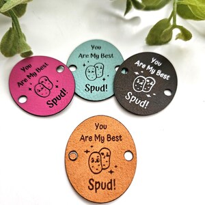 Peut inclure: Quatre étiquettes rondes en cuir de couleurs rose, turquoise, marron et beige, avec le texte "You Are My Best Spud!" et un dessin de pomme de terre. Chaque étiquette a deux trous pour la fixation.