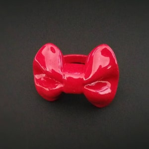 May include: A red plastic ring with a bow design. The bow is shiny and has a glossy finish.
