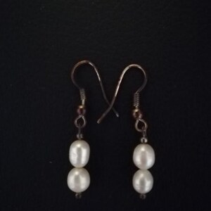 May include: A pair of silver dangle earrings with two white pearl beads on each earring.