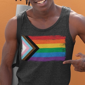 Könnte beinhalten: Eine Person trägt ein dunkelgraues Tanktop mit einem Regenbogen-Pride-Flaggen-Design. Die Flagge zeigt ein schwarzes und braunes Dreieck mit einem weißen und hellblauen Dreieck darin, gefolgt von einem gelben, orangen, roten, grünen, blauen und violetten Streifen.