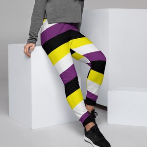 May include: A person wearing a gray cropped sweatshirt and black, white, yellow, and purple striped sweatpants. The sweatpants have a diagonal stripe pattern.