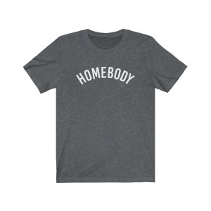 May include: A dark heather grey t-shirt with the word "HOMEBODY" printed in white in an arched font.