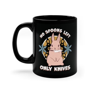 Pode incluir: Caneca de café preta com um gráfico branco de um coelho rosa segurando uma faca. O gráfico é cercado por um círculo com o texto "No Spoons Left Only Knives".