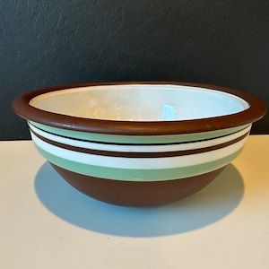 Puede incluir: Un tazón de cerámica marrón con rayas blancas y verdes. El tazón está vacío y tiene un interior blanco.