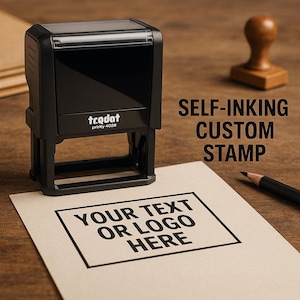 May include: A black self-inking custom stamp with the text "Your Text or Logo Here" printed on a beige paper. The stamp is next to a pencil and a wooden stamp handle on a wooden surface. The stamp has the text "trodat" and "printy 4028".