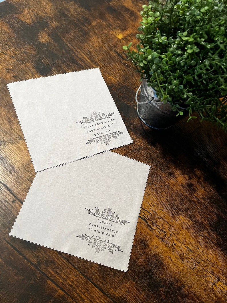 May include: Two white microfiber cloths with black floral designs and inspirational quotes. The top cloth reads "FULLY ACCOMPLISH YOUR MINISTRY 2 TIM. 4:15". The bottom cloth reads "CUMPLE COMPLETAMENTE TU MINISTERIO 2 TIM. 4:15".