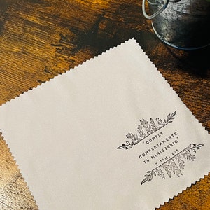 May include: A white microfiber cleaning cloth with a black floral design and the text "# Cumple Completamente Tu Ministerio" 2 Tim. 4:5.