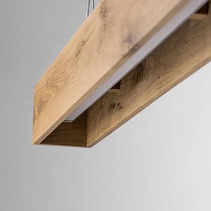 May include: A rectangular wooden pendant light fixture with a white light source inside. The fixture is made of natural wood with a light brown finish.