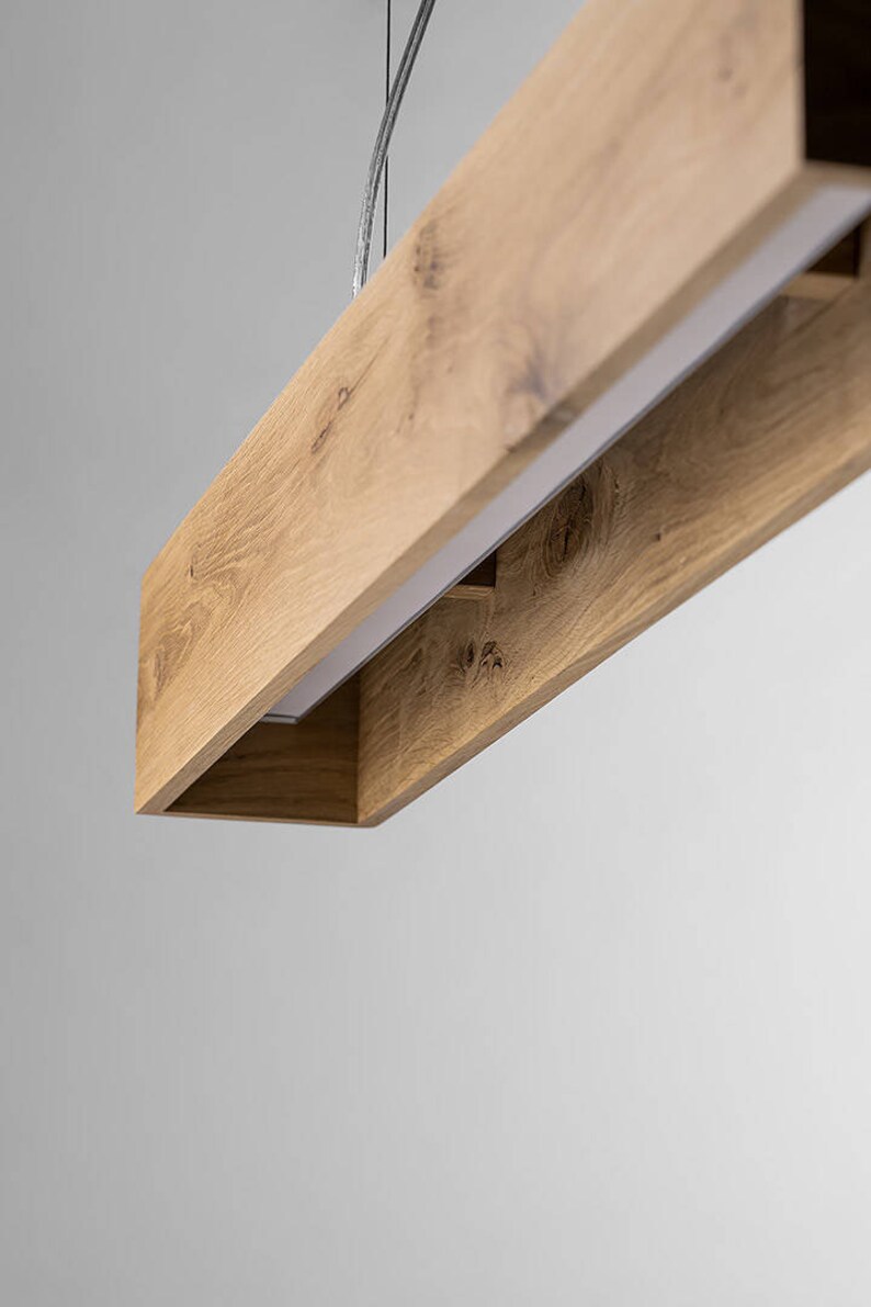May include: A rectangular wooden pendant light fixture with a white light source inside. The fixture is made of natural wood with a light brown finish.