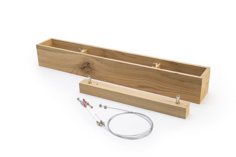 May include: A wooden box with two separate pieces, a long rectangular box and a shorter rectangular piece. The box is made of light brown wood with a natural grain pattern. The box is disassembled and laid out on a white surface. The box is designed to be used as a light fixture.