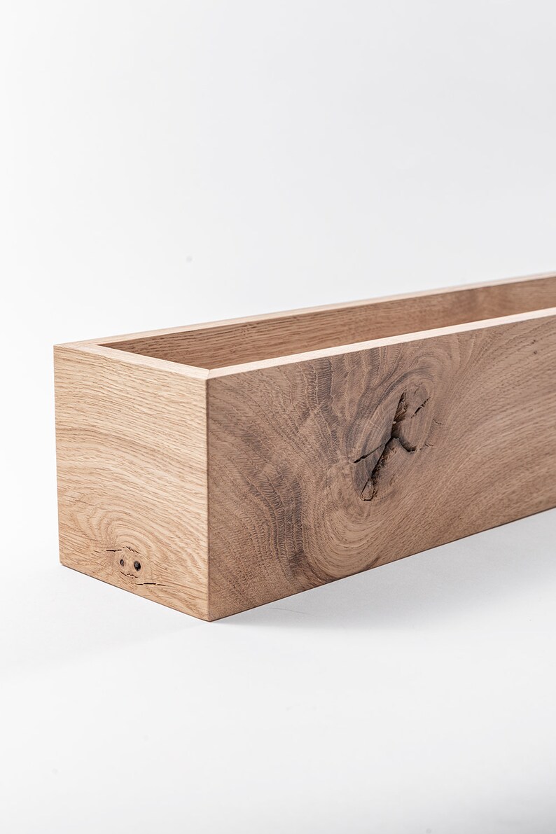 May include: A rectangular wooden planter box with a natural wood finish. The planter has a knot in the wood on the front side.