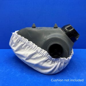 May include: A gray and black CPAP mask with a white fabric cover. The mask has a small fan on the side. "Cushion not included" is written below the mask.