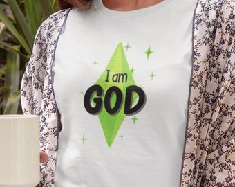 May include: White t-shirt with the text "I am GOD" in black and green. The text is centered on a green diamond shape. The person is wearing a floral patterned kimono and holding a white mug.