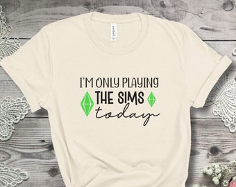 May include: A natural coloured t-shirt with the text "I'm only playing The Sims today" and a green diamond graphic.