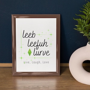 May include: Framed print with the words "leeb leefuh lurve" in a whimsical font, with a green diamond and star accents. The phrase "Live, Laugh, Love" is printed below. The frame is brown.