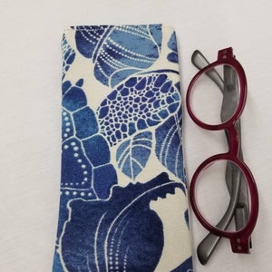 K&ouml;nnte beinhalten: Ein Brillenetui aus blau-wei&szlig;em Stoff mit einer roten und grauen Lesebrille daneben.