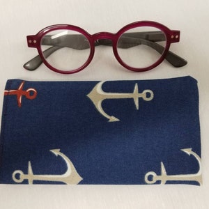 K&ouml;nnte beinhalten: Ein rundes rotes Brillenetui mit einem blauen Ankerdruck. Das Etui ist aus Stoff und hat einen Rei&szlig;verschluss.