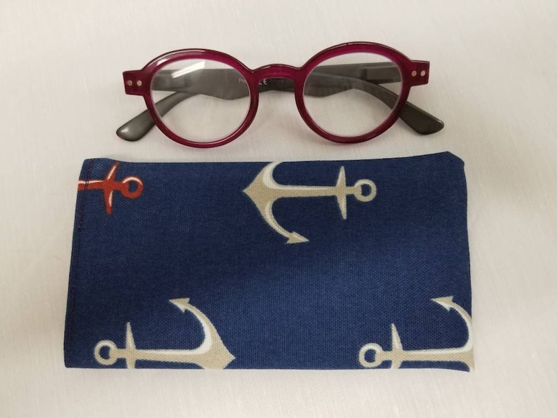K&ouml;nnte beinhalten: Ein rundes rotes Brillenetui mit einem blauen Ankerdruck. Das Etui ist aus Stoff und hat einen Rei&szlig;verschluss.