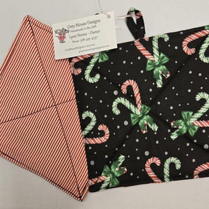 May include: A pair of black and white pot holders with a candy cane pattern. The pot holders are made of fabric and have a loop for hanging. The text on the tag reads "Grey Mouse Designs Handmade in the USA Lynn Noone - Owner Phone 518-439-4337 GreyMouseDesigns.etsy.com greymousedesigns@gmail.com"