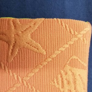 May include: Orange fabric with a textured pattern of starfish and rope. The fabric has a green border.
