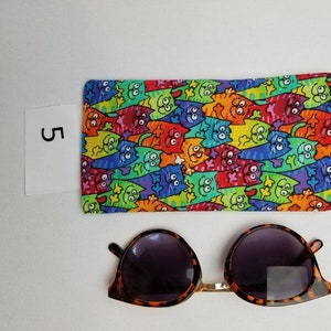 K&ouml;nnte beinhalten: Ein farbenfrohes Etui mit Katzenmotiv f&uuml;r Brillen mit einer Sonnenbrille aus Schildpatt mit dunklen Gl&auml;sern.