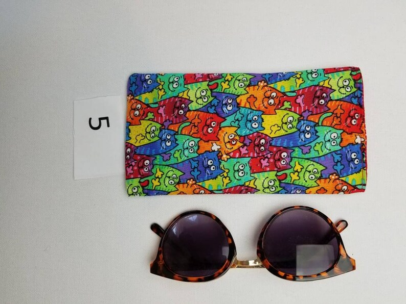 K&ouml;nnte beinhalten: Ein farbenfrohes Etui mit Katzenmotiv f&uuml;r Brillen mit einer Sonnenbrille aus Schildpatt mit dunklen Gl&auml;sern.