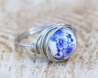 May include: A silver wire wrapped ring with a blue and white porcelain cabochon featuring a floral design.