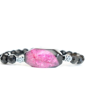 Könnte beinhalten: Ein schwarzes Perlenarmband mit einem rosafarbenen und schwarzen Achat-Anhänger.