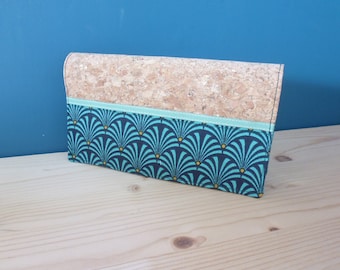 May include: A teal and gold patterned fabric wallet with a cork top and a light green ribbon.