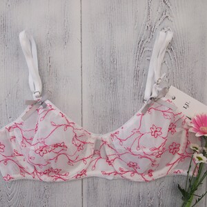 May include: White lace bra with pink floral print and adjustable straps. The bra has a delicate floral pattern and a soft, feminine look.