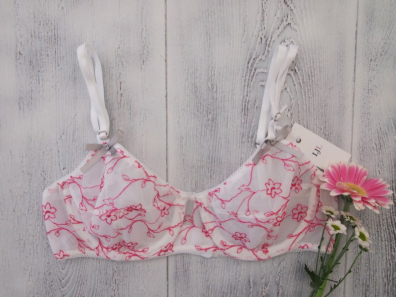 May include: White lace bra with pink floral print and adjustable straps. The bra has a delicate floral pattern and a soft, feminine look.
