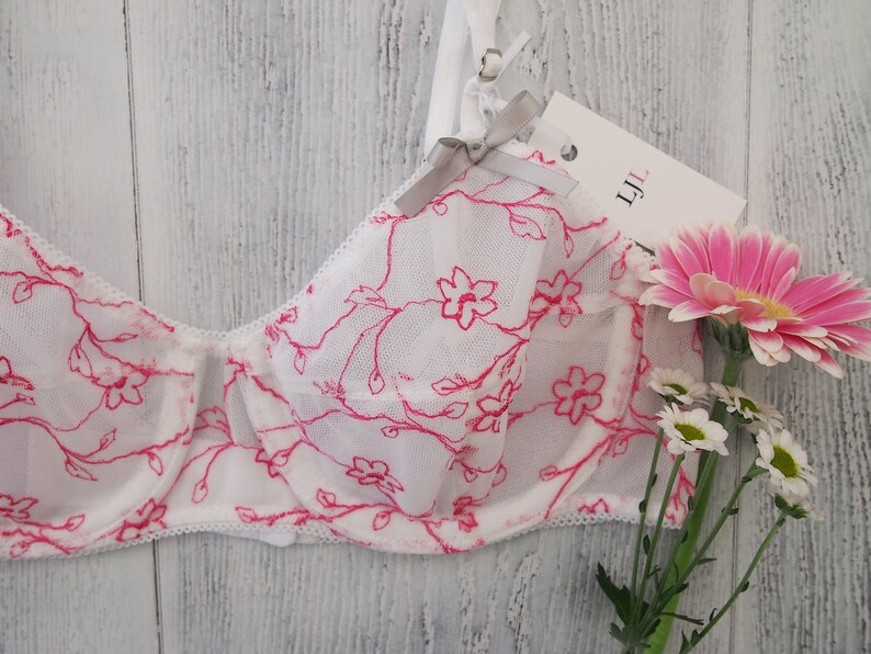 May include: White lace bra with pink floral embroidery and a gray bow. The bra has a tag that says "LJL".