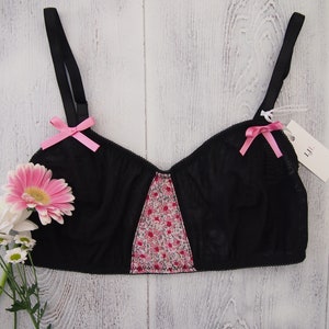 May include: Black lingerie bra with pink ribbon accents and a floral print panel. The bra has adjustable straps and a delicate lace design.