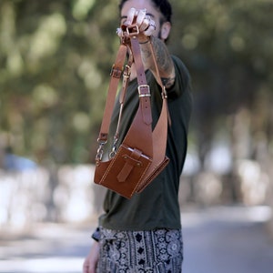 May include: A brown leather crossbody bag with adjustable straps and a flap closure. The bag has a small pocket on the front and a larger pocket on the back.