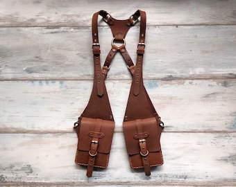 May include: Brown leather harness with two attached pouches. The harness has adjustable straps and metal buckles. The pouches have a flap closure with a metal buckle.